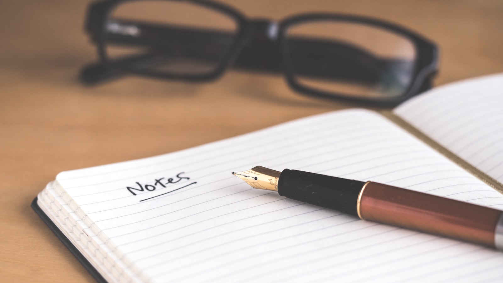 A hand writing a checklist in a notebook next to a cup on a wooden table.