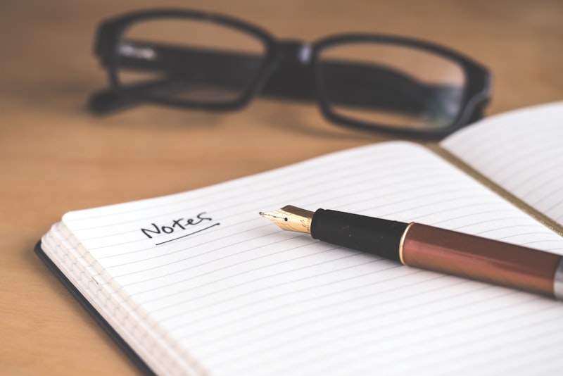 A hand writing a checklist in a notebook next to a cup on a wooden table.